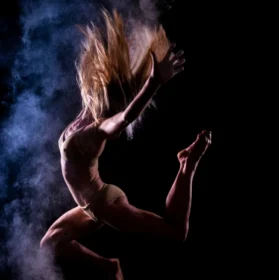 Photo d'une danseuse en avec de la fumée bleue et mauve sur la gauche de l'image mais en face de la danseuse