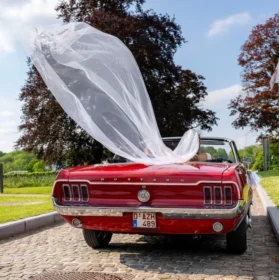 Mariés dans une ancienne Ford Mustang avec le voile de la mariée qui prend le vent