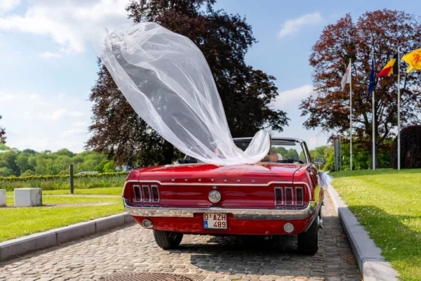 Mariés dans une ancienne Ford Mustang avec le voile de la mariée qui prend le vent